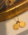 Gold necklace with two engraved pendants on a reflective surface