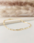 A gold-filled paperclip bracelet laid out on a flat surface with a furry object in the background.