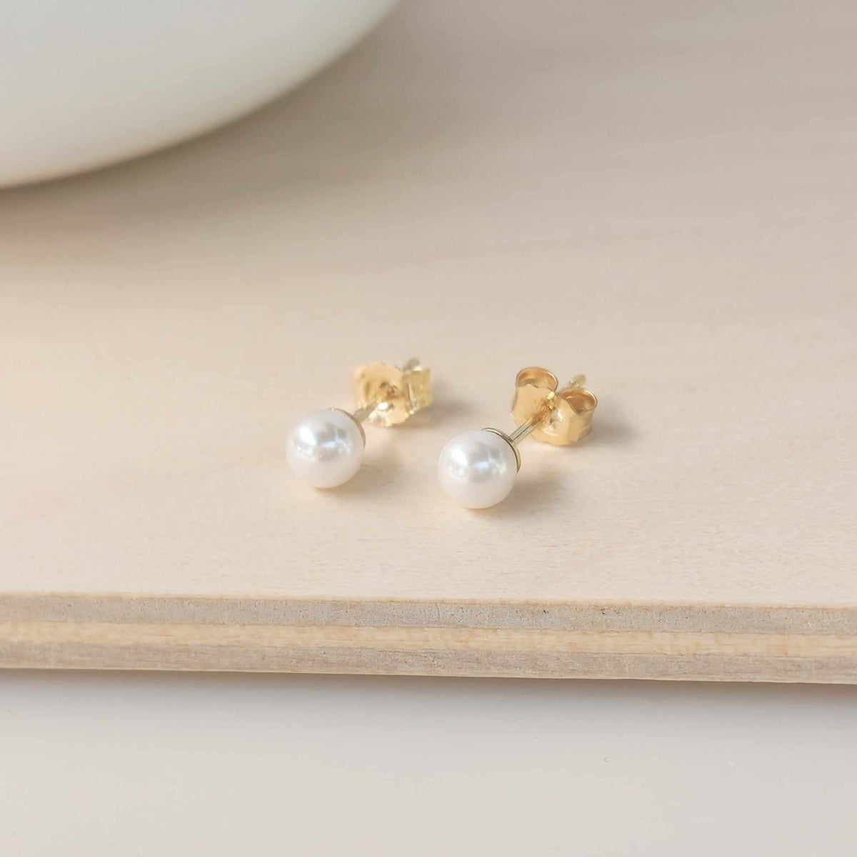 Close-up of classic 4mm crystal pearl stud earrings with 14K yellow gold backing and post