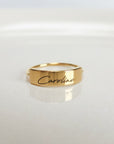 A gold-colored ring with the name 'Caroline' engraved on it, displayed on a white surface.