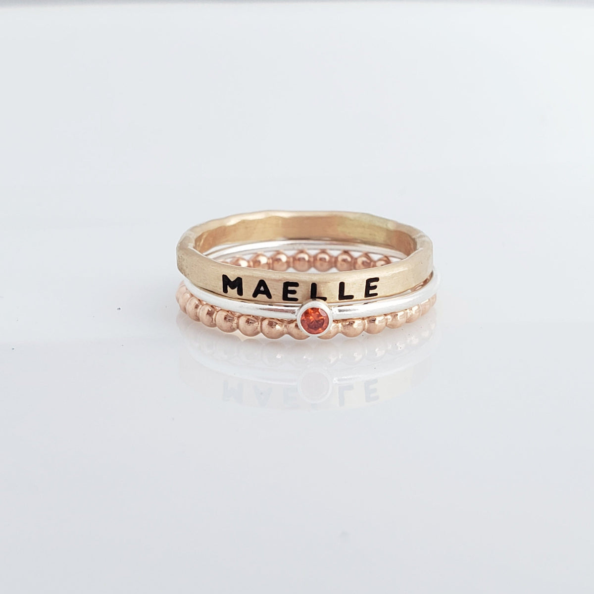 Three handmade Polly Stacking Rings in yellow gold, sterling silver, and rose gold, displayed stacked together.