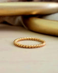A thin twisted gold stacking ring displayed on a surface.