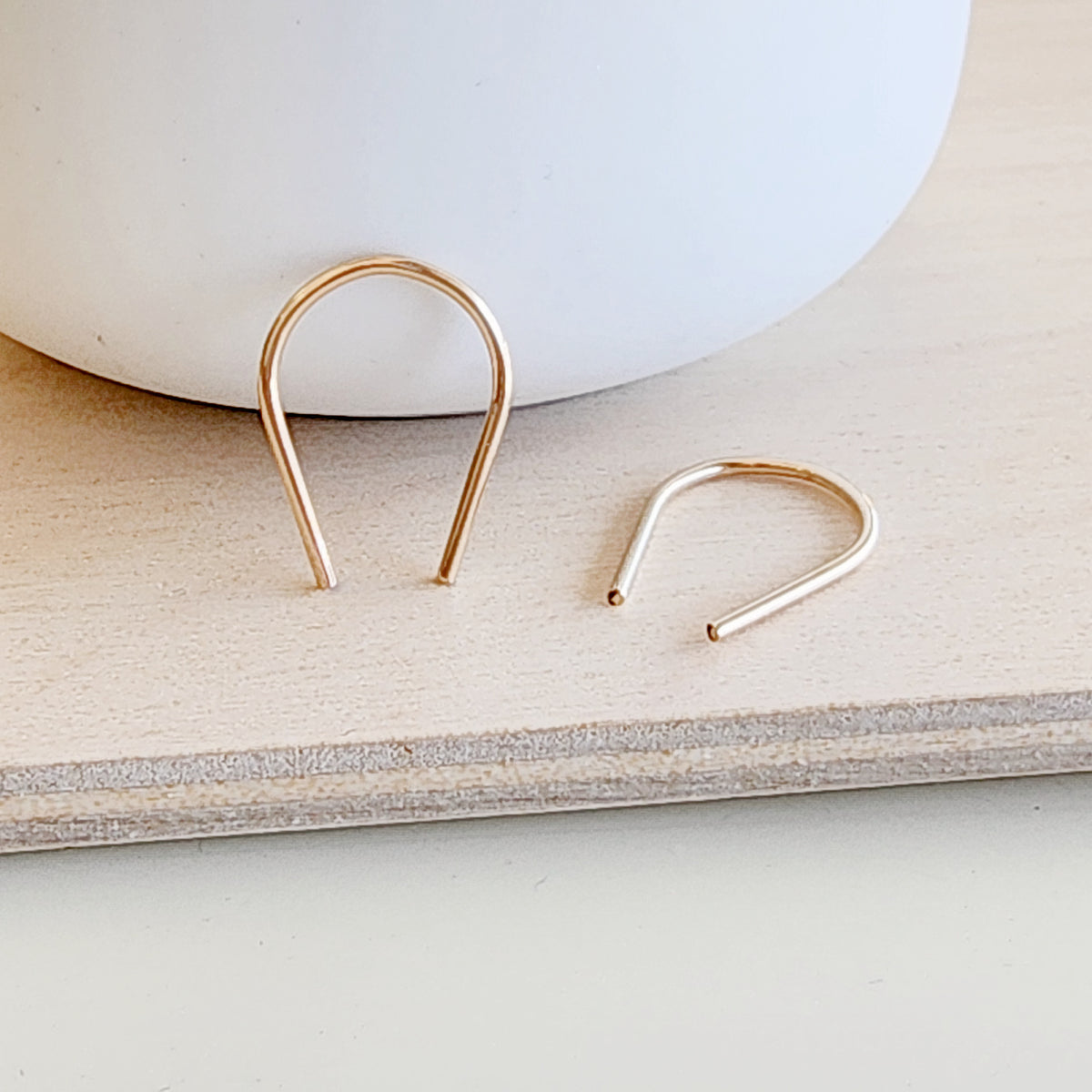 Modern flat lay of gold U-shaped earrings next to ceramic bowl