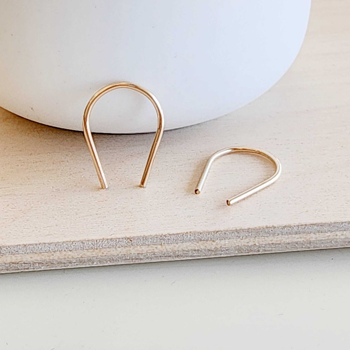 Modern flat lay of gold U-shaped earrings next to ceramic bowl