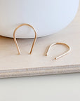 Modern flat lay of gold U-shaped earrings next to ceramic bowl