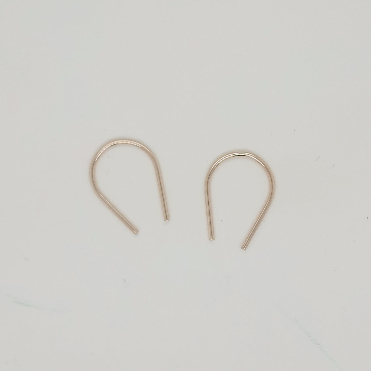 Gold U-shaped minimalist earrings displayed on white surface