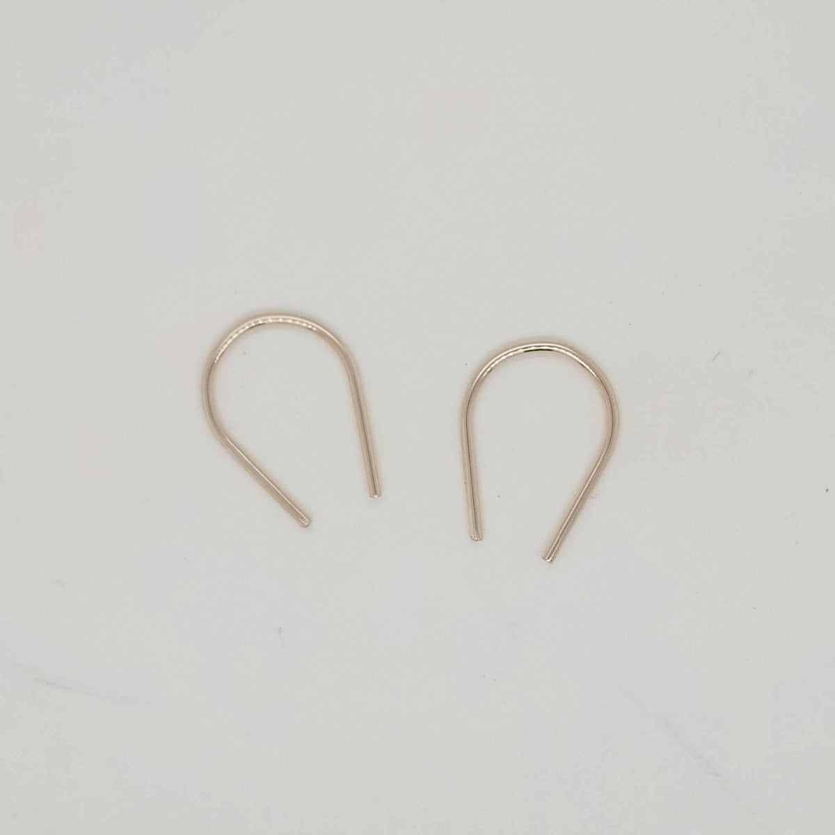 Gold U-shaped minimalist earrings displayed on white surface