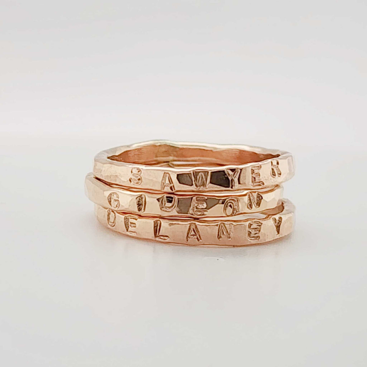 three handmade stacking rings stacked together and personalized with 'SAWYER', 'GIDEON', and 'DELANEY'