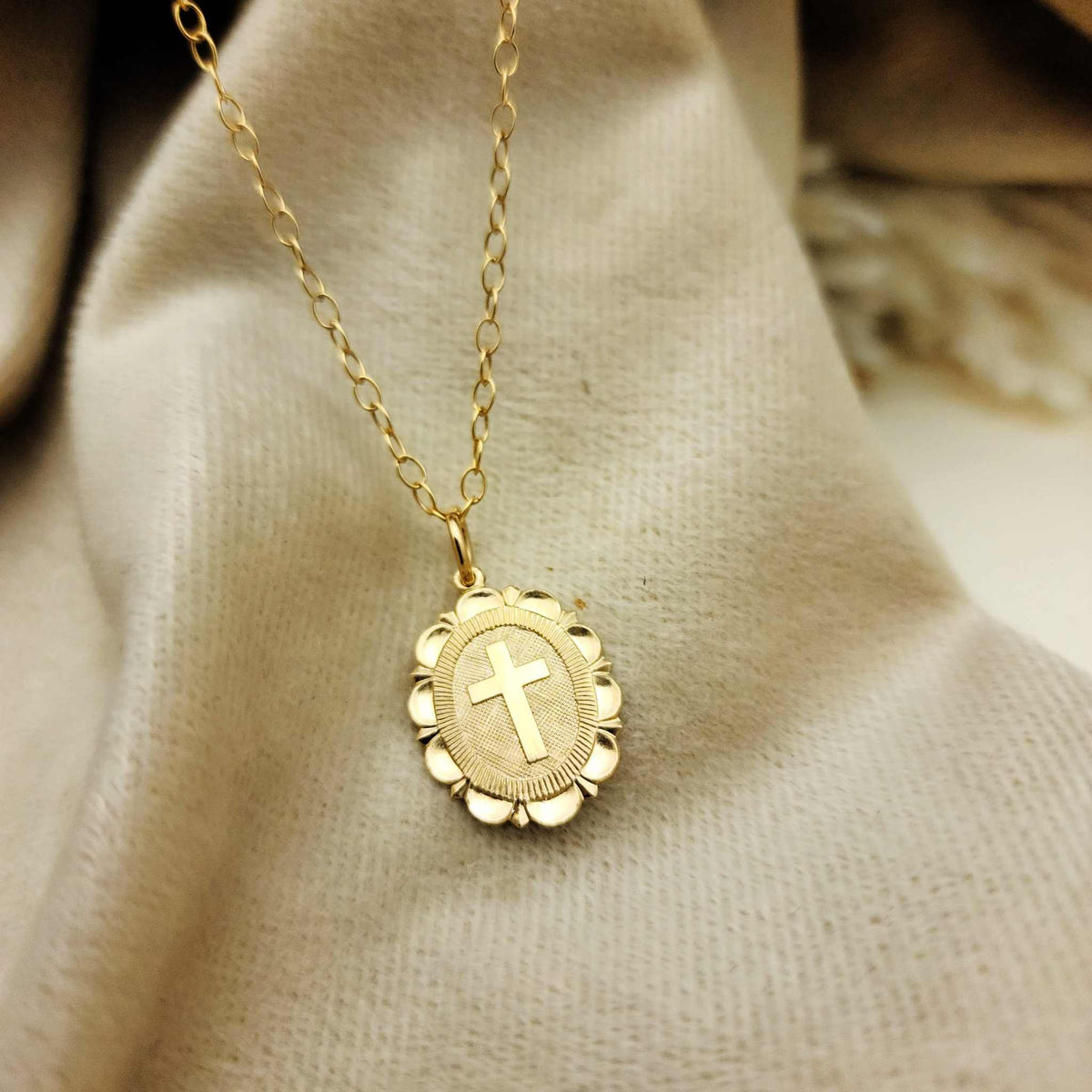Gold necklace with a cross pendant on a beige fabric background