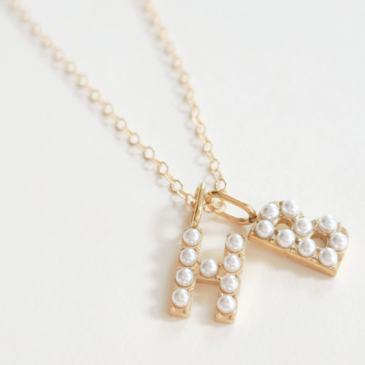 Gold necklace with a letter 'H' and "B" pendant on a light background