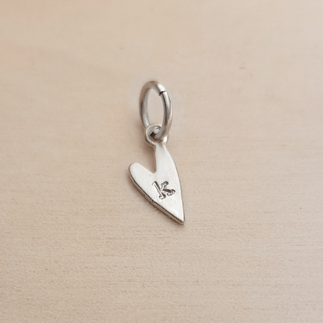 Silver heart-shaped pendant with a letter 'K' on a beige background