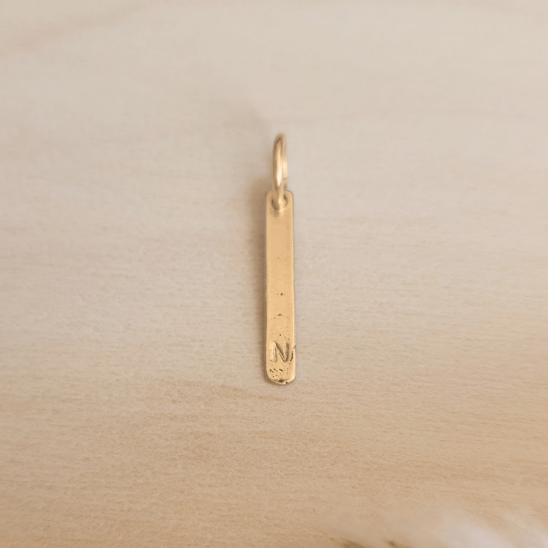 silver pendant with engraved letter 'N' on a beige background