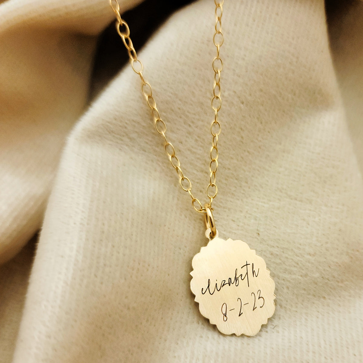 Gold necklace with a engraved pendant on a beige fabric background