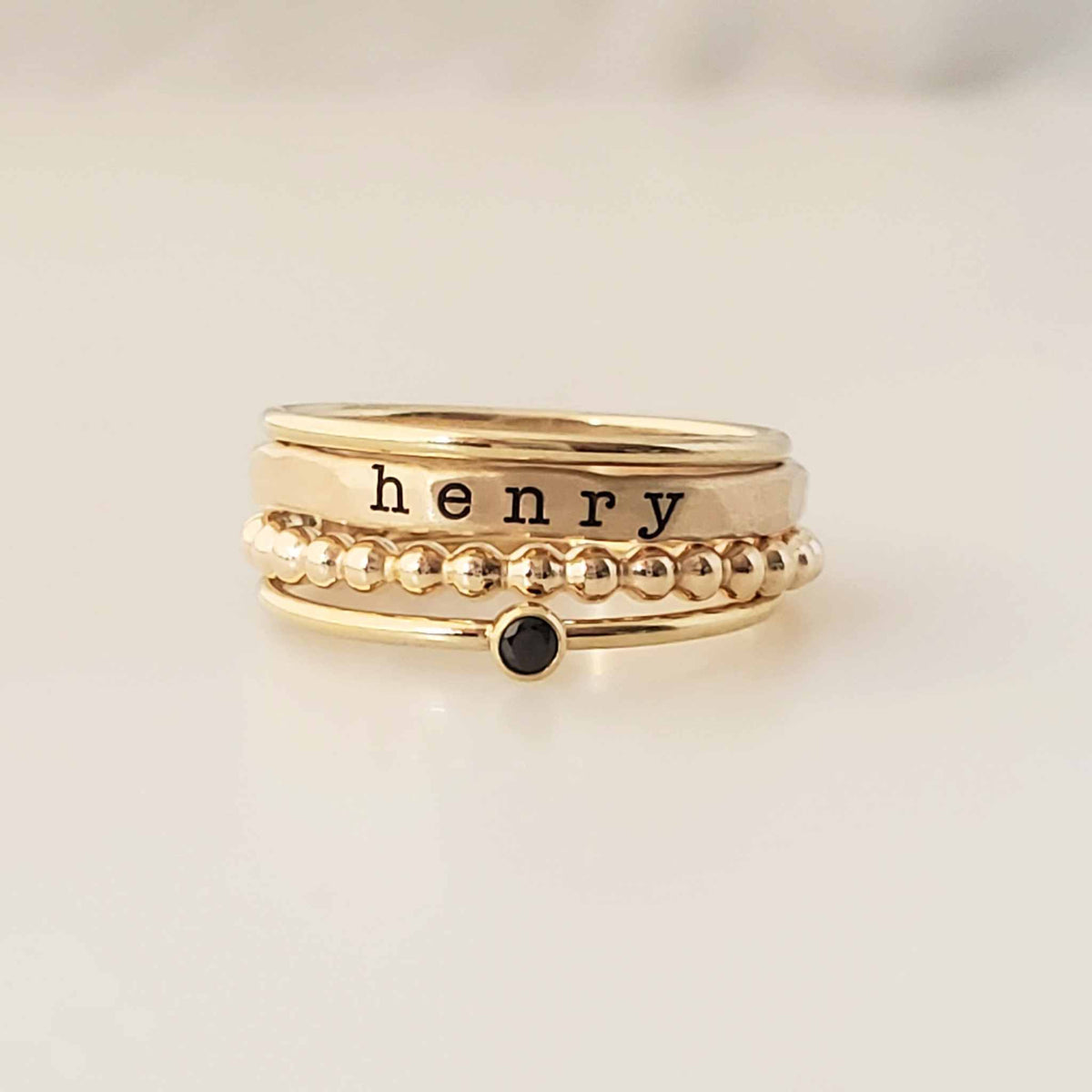 The Everly Ring Set featuring personalized 14K gold-filled stacking rings with name, beaded spacer, plain band, and birthstone ring options