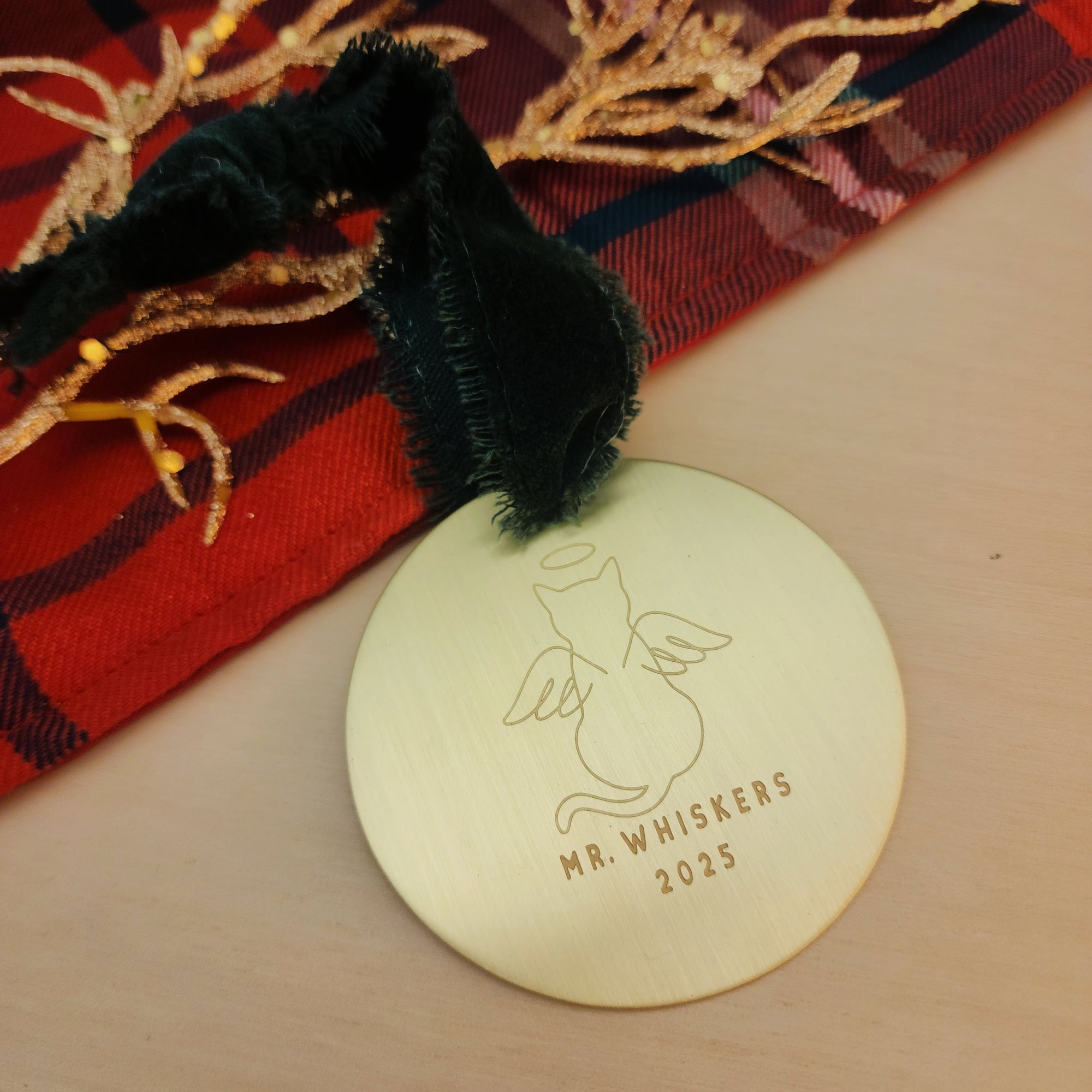 Round gold tag with engraved text and a cat illustration on a wooden surface with decorative elements.