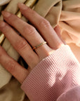 2mm yellow gold stacking ring on the middle finger of a woman with a name engraved on the ring. Woman is wearing a pink sweatshirt with long pink nails.