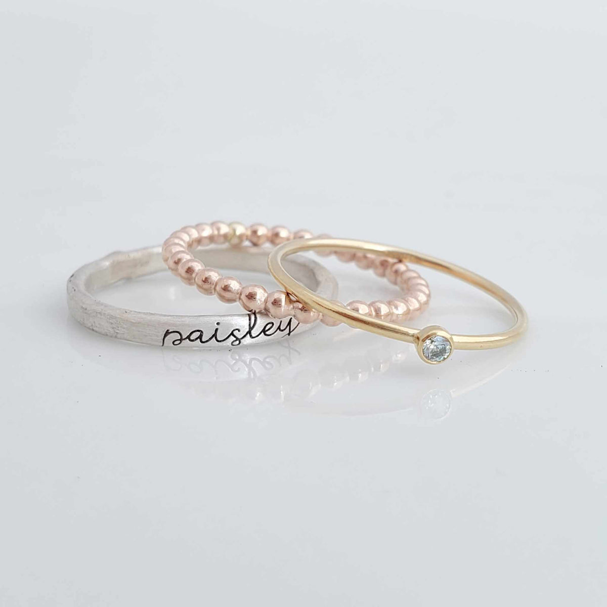 Violet mixed metals birthstone ring set with personalized silver name ring, gold birthstone ring, and rose gold beaded ring stacked together