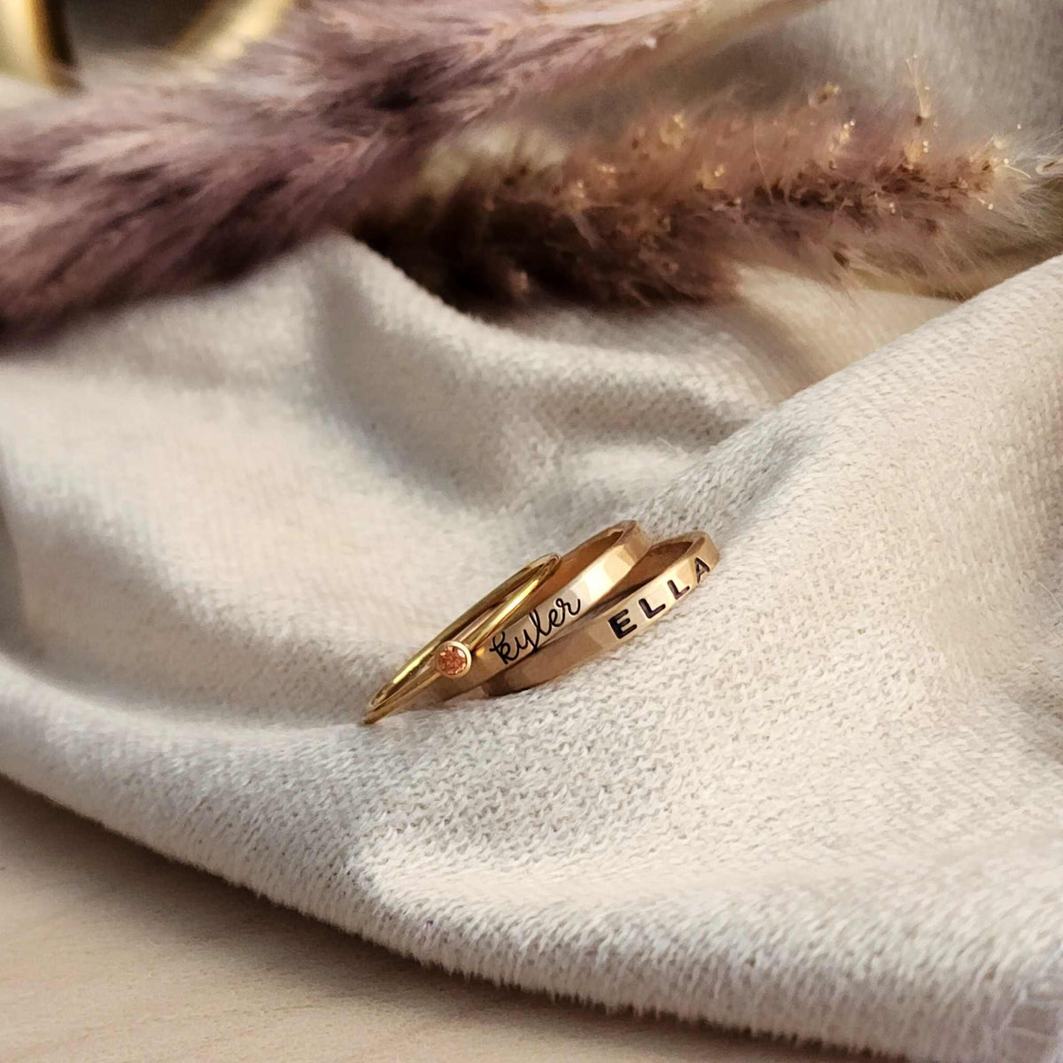 a set of three gold filled rings, including two name rings and one birthstone ring, displayed on a white cloth