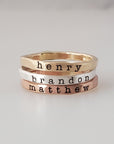 Three stacked rings made of different metals, with the names 'henry', 'brandon', and 'matthew' engraved on them, displayed on a white surface.