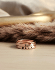A set of stackable rose gold filled rings, with one clear cz ring and two personalized name rings, displayed on a wooden surface.
