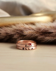 A set of stackable rose gold filled rings, with one clear cz ring and two personalized name rings, displayed on a wooden surface.