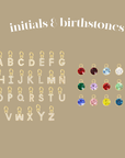 Gold letter pendants with birthstone colors on a beige background