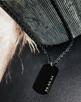 Black dog tag necklace with engraved date on a textured surface