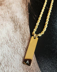 Gold necklace with a bar pendant featuring an 'A' on a textured surface.