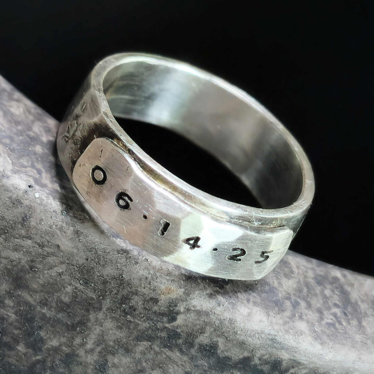 Silver ring with engraved date on a dark background