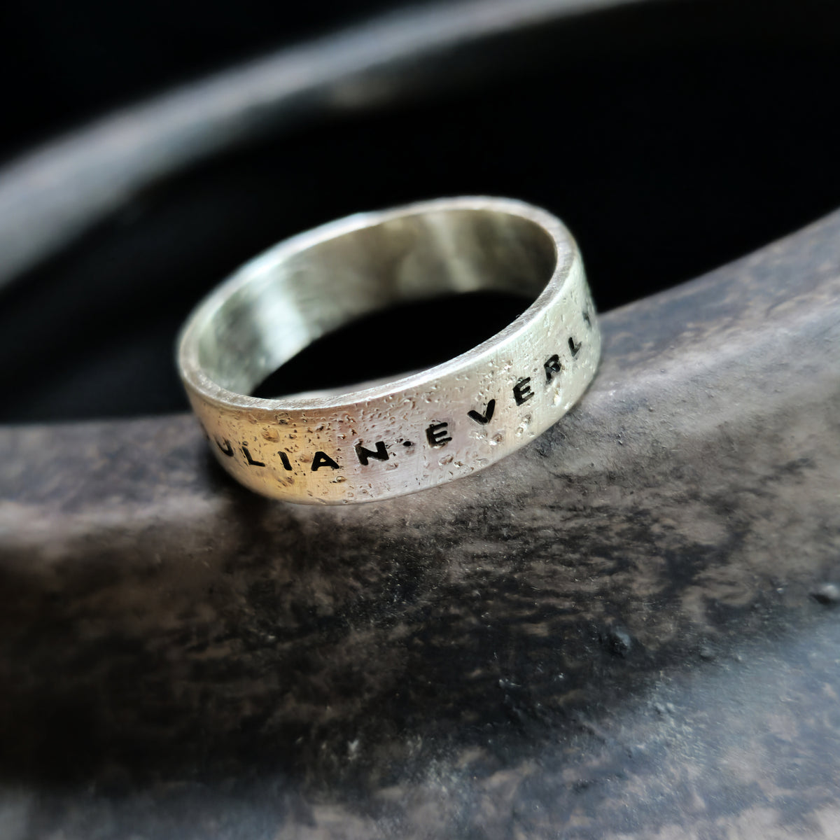 Silver ring with engraved text on a dark stone surface
