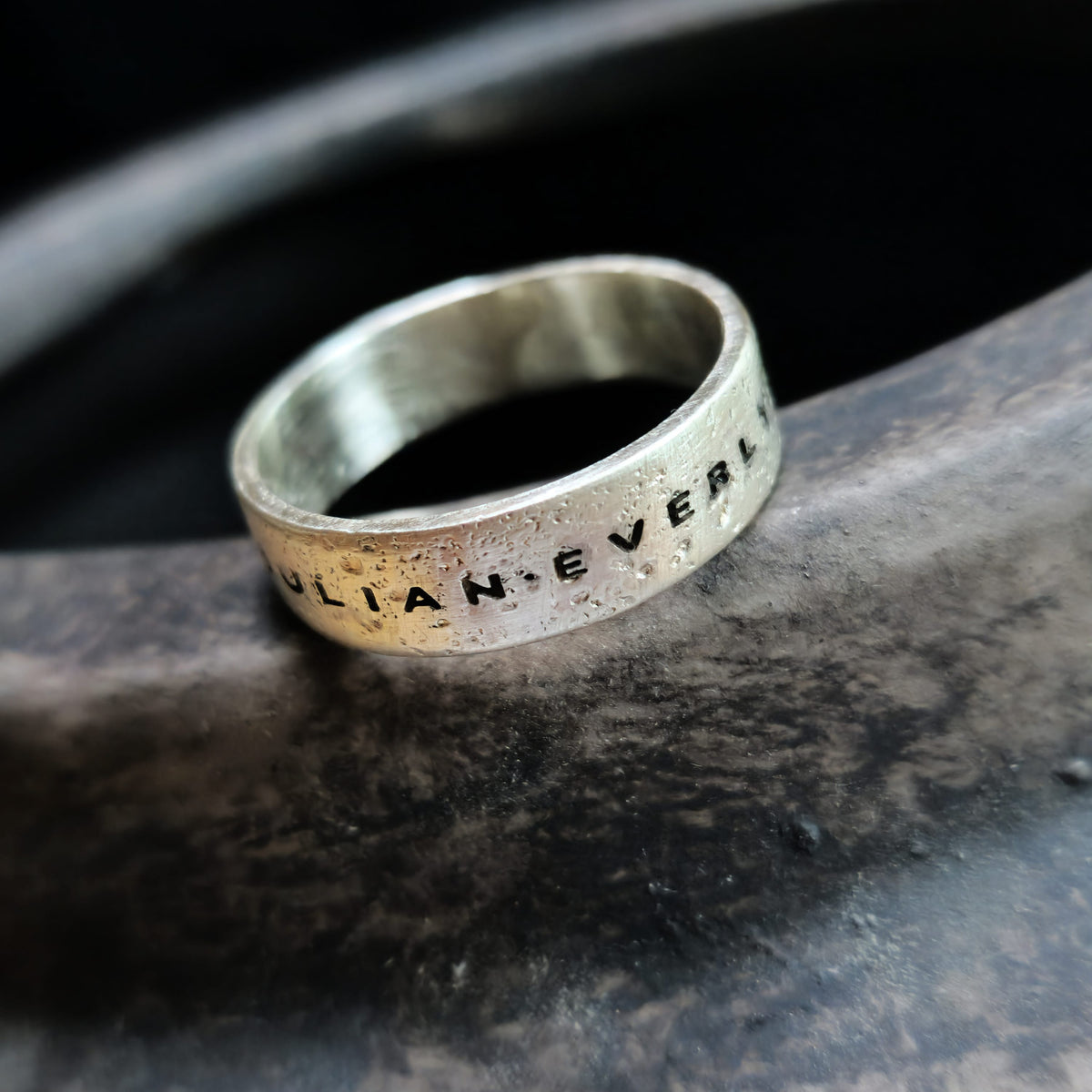 Silver ring with engraved text on a dark stone surface