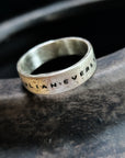 Silver ring with engraved text on a dark stone surface