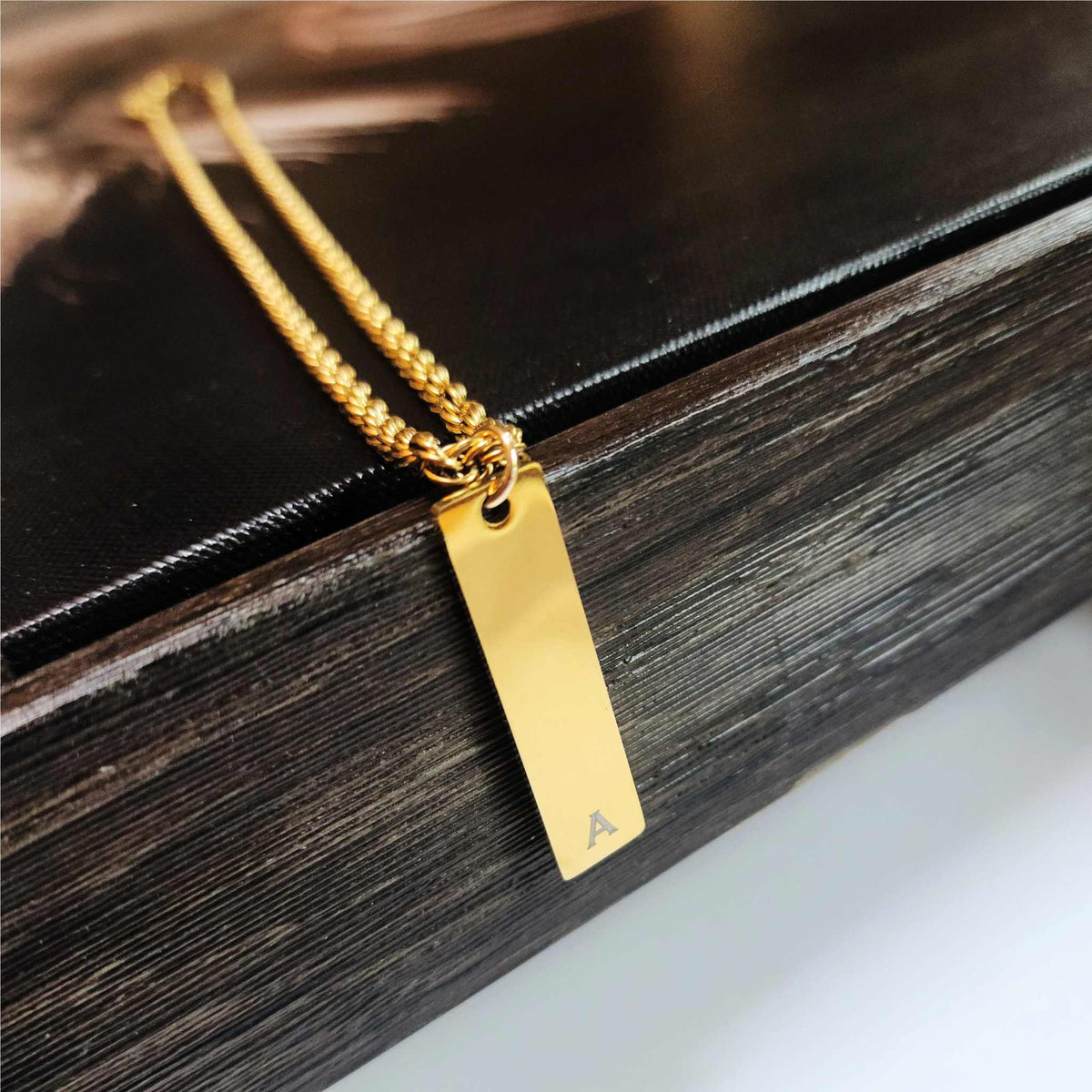 Gold necklace with a rectangular pendant on a wooden surface