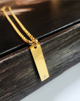 Gold necklace with a rectangular pendant on a wooden surface