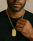 Man wearing a gold necklace with a dog tag against a neutral background