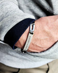 Close-up of a person wearing a silver bracelet with brand engraving.