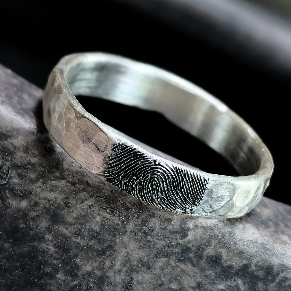 Silver ring with fingerprint engraving on a dark stone surface