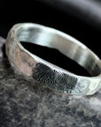 Silver ring with fingerprint engraving on a dark stone surface