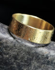 Gold ring with textured surface on a dark stone background
