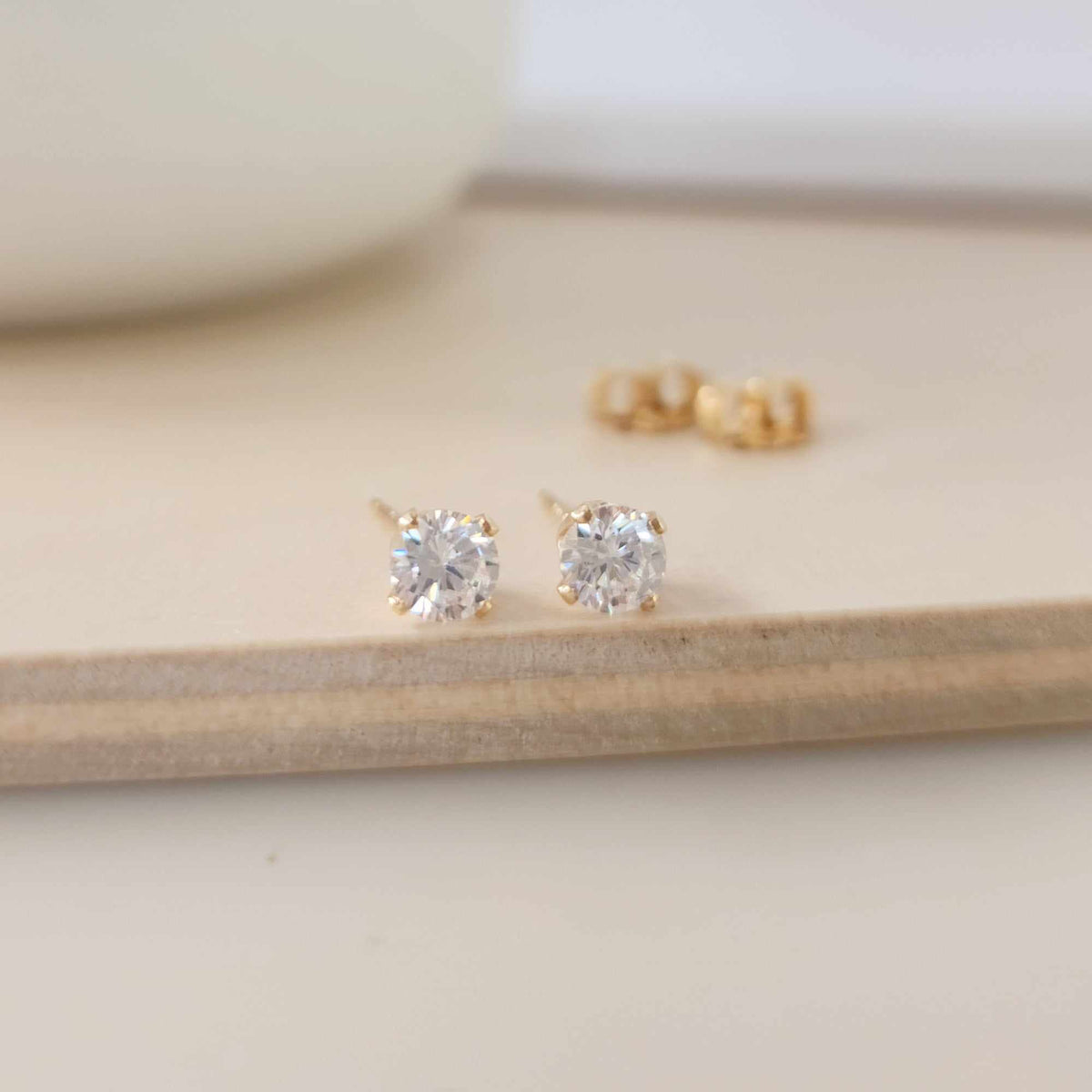 A pair of clear cubic zirconia stud earrings in gold settings, displayed on a wooden surface.