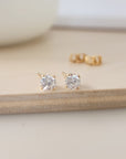 A pair of clear cubic zirconia stud earrings in gold settings, displayed on a wooden surface.
