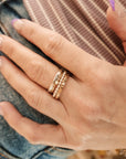 A set of four stackable rings on a white surface, including a sterling silver beaded ring, a fine silver name ring, and two 14K gold-filled rings, one with a birthstone and one with a name engraved.