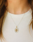 Close-up of a gold necklace with an oval pendant worn by a person against a white background
