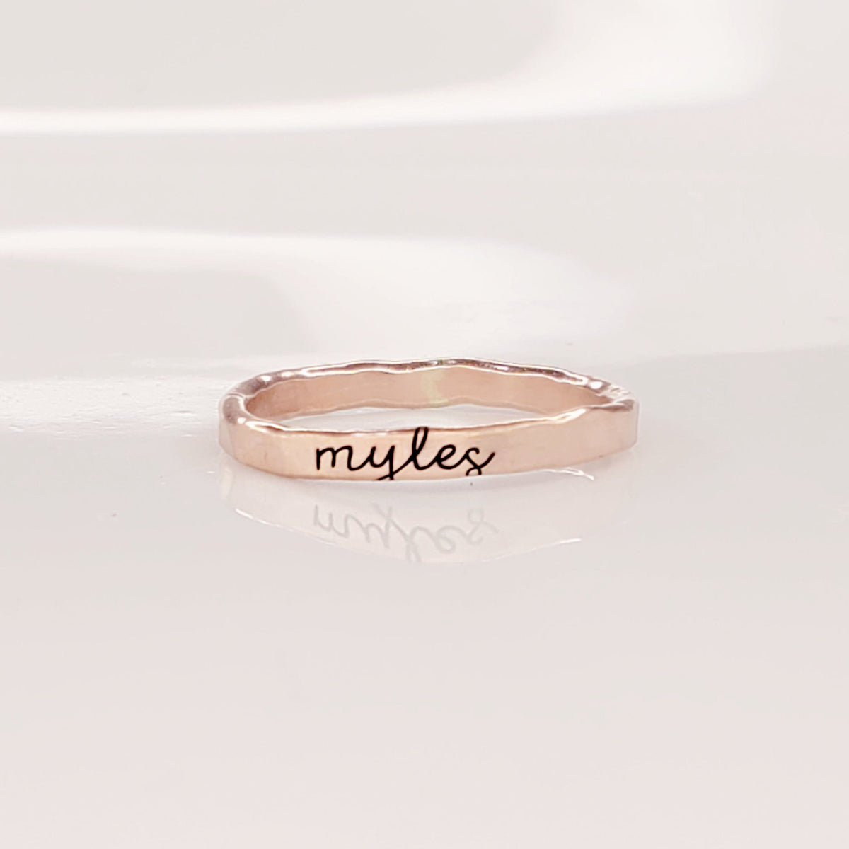 A gold-colored thin ring with cursive script engraving on a white background.
