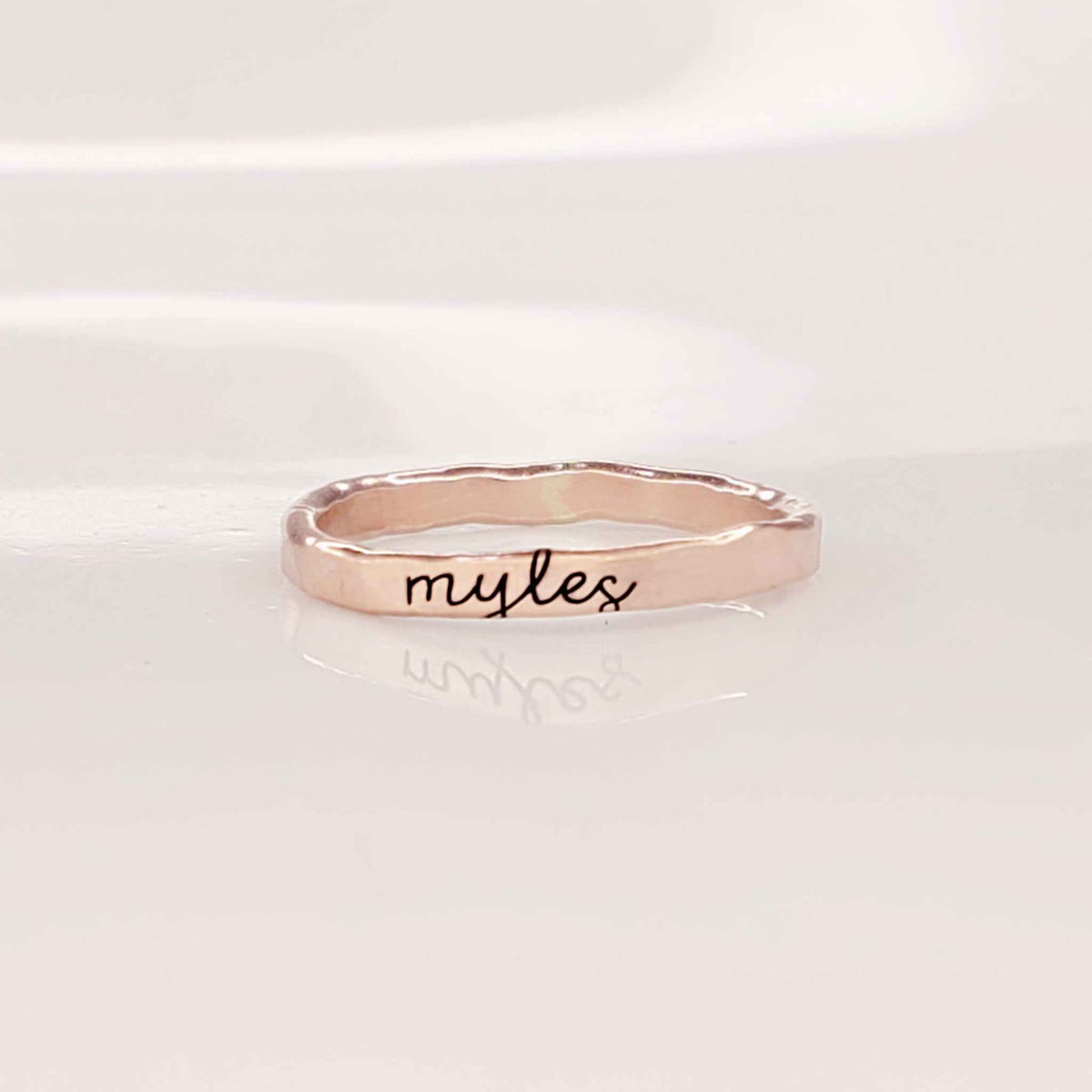 A gold-colored thin ring with cursive script engraving on a white background.