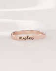 A gold-colored thin ring with cursive script engraving on a white background.