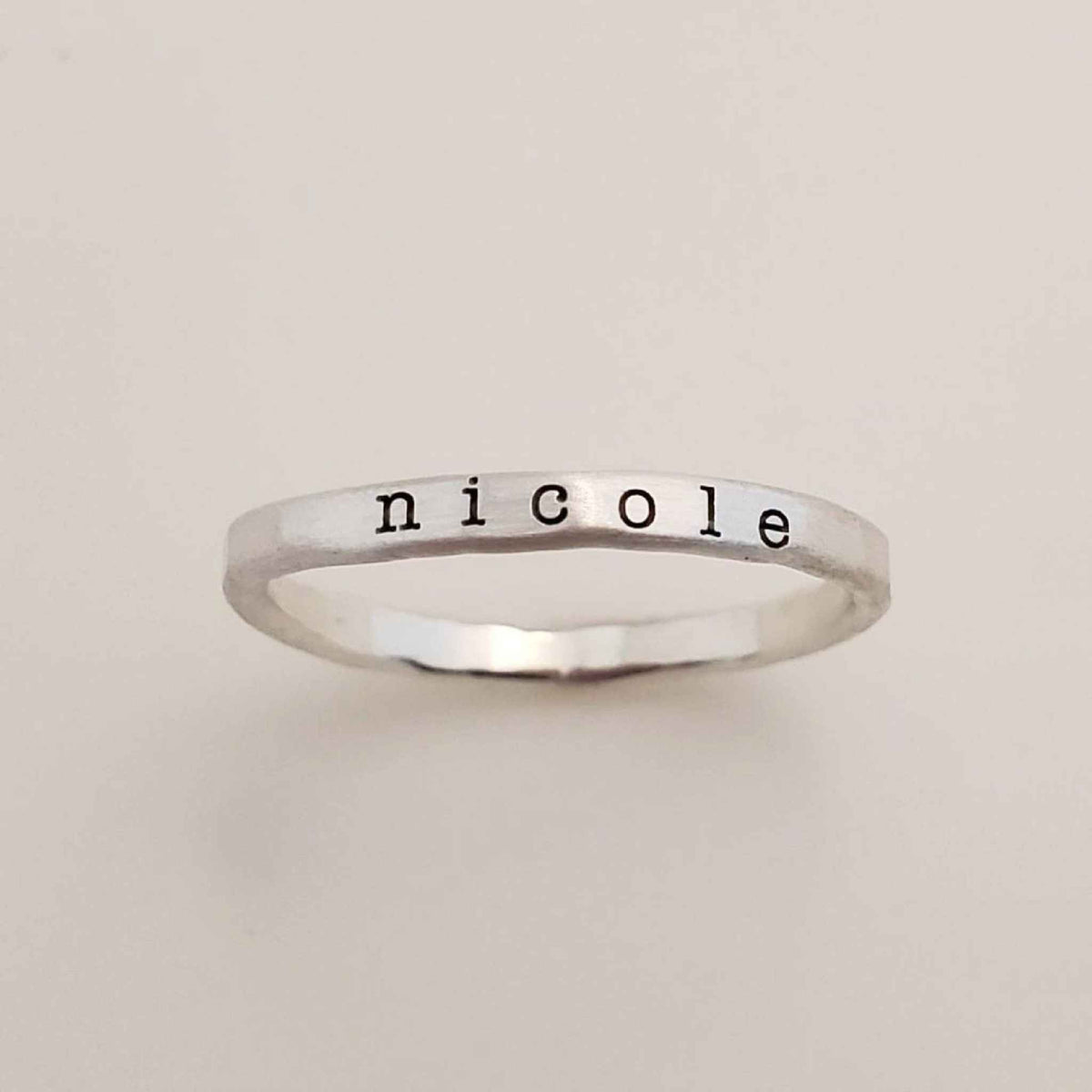 A gold-colored ring with the name 'nicole' engraved in a typewriter-style font.