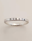 A gold-colored ring with the name 'nicole' engraved in a typewriter-style font.