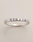 A gold-colored ring with the name 'nicole' engraved in a typewriter-style font.
