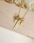 Overhead view of gold memorial necklace with “Michael” engraved bar, heart charm, angel wing charm, and birthstone on wood.